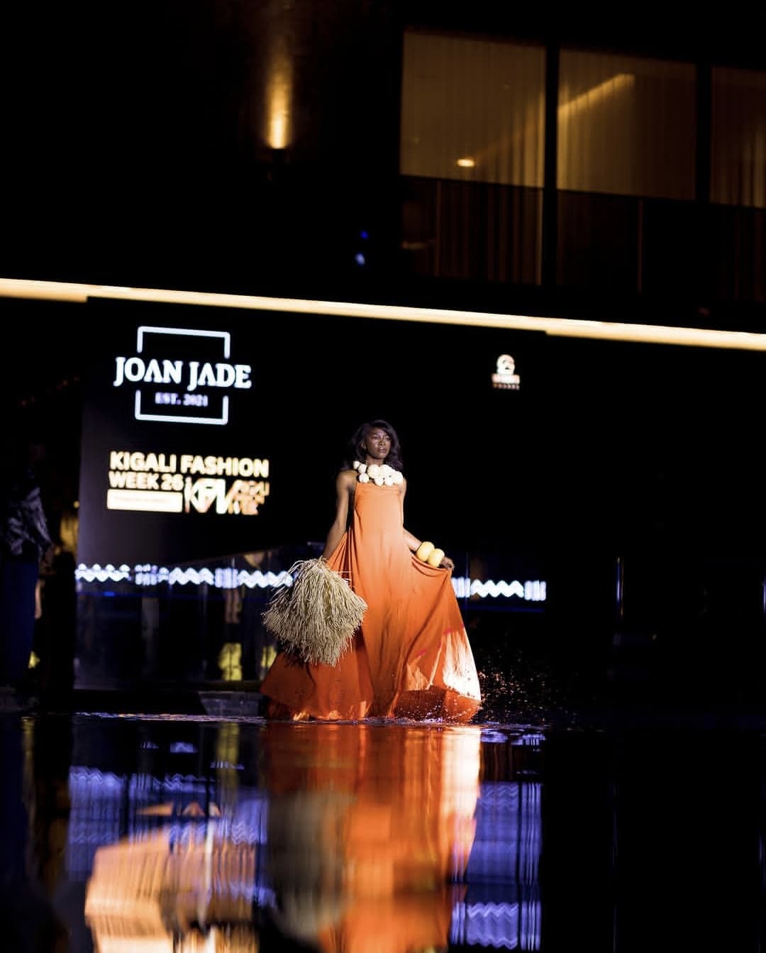 A model in a flowing orange gown on a night runway