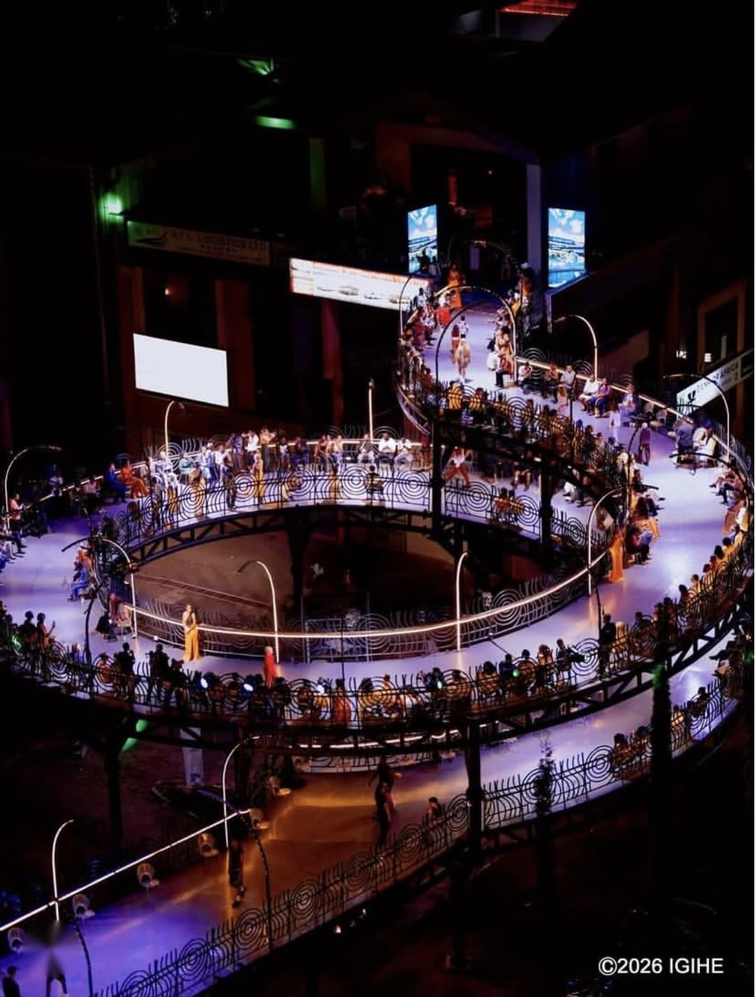 A spiral runway lit in violet at night, lined with guests